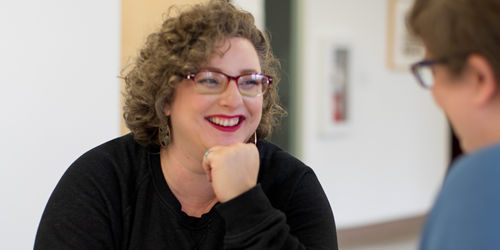 A woman smiling while chatting with another person who is out of focus.